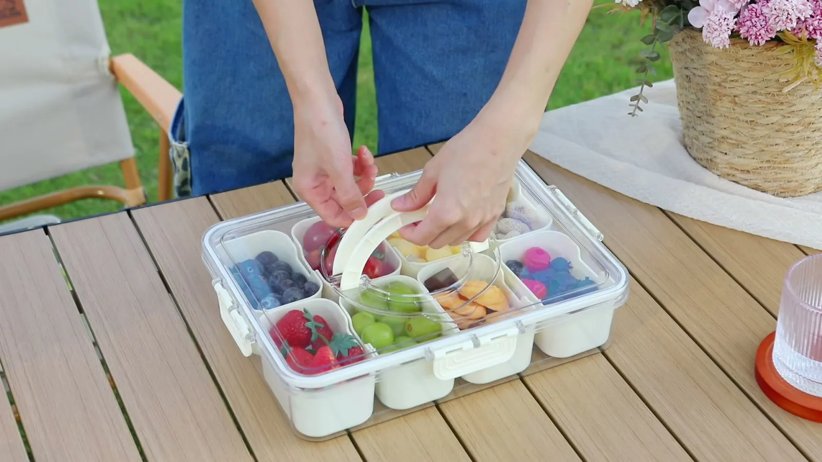 Manos que llevan un Snackle Box por el asa hacia una mesa en el jardín